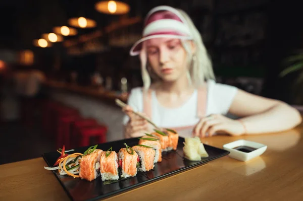 Assiette de rouleaux de sushi au restaurant sur fond de fille en vêtements roses. Photo de nourriture de sushi et visiteur du restaurant photographié. Fille manger un délicieux ensemble de sushis dans un bar à sushis . — Photo