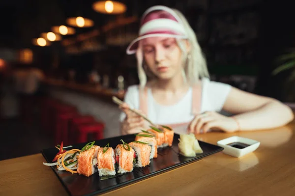 Pembe giysiler içinde kız arka plan üzerinde restoranda suşi rulo tabak. Suşi ve restoran ziyaretçinin gıda fotoğrafı resimde. Kız bir suşi barda suşi lezzetli bir dizi yemek. — Stok fotoğraf