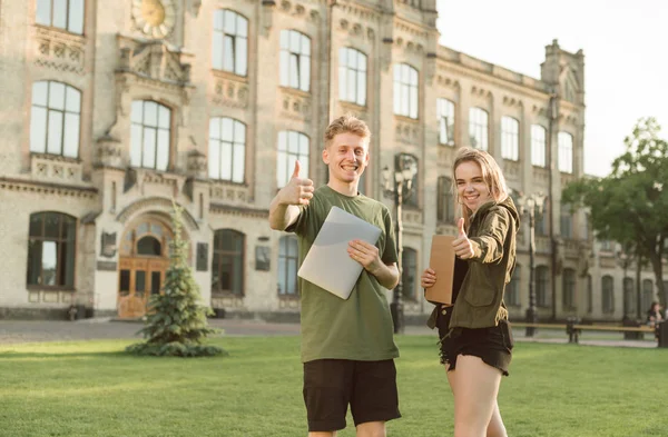 Dois estudantes alegres com sorrisos largos levantando os polegares se sentir — Fotografia de Stock