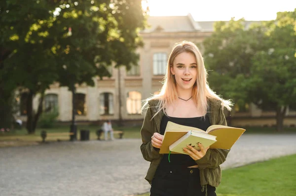 Sorprendida joven y hermosa estudiante posando en el parque universitario al aire libre sosteniendo libros y cuadernos. Atractivo estudiante lindo gratamente sorprendido de las calificaciones positivas en la universidad . —  Fotos de Stock