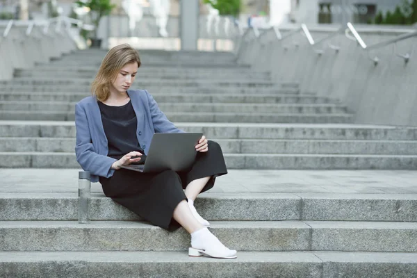 Dizüstü bilgisayarında çalışan konsantre bir genç iş kadınının portresi. Bilgisayarda mesajları kontrol merdivenlerde oturan meşgul kadının yanında su şişesi. — Stok fotoğraf