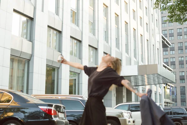 Blurred portrait, focus on background. Carefree young happy girl on street, eyes closed with enjoyment, breathing at full outside and feeling free. Cheerful lady feeling successful near skyscraper.