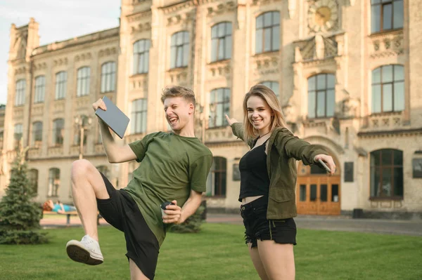 Dos estudiantes emocionados con exámenes aprobados en la calle sintiéndose satisfechos, felices y orgullosos. Alegre pareja de estudiantes celebrando aprobado evaluación cerca del edificio de la universidad en el parque . Fotos De Stock