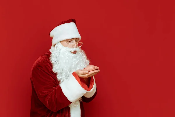 Retrato de Santa de pie sobre fondo rojo mira las manos levantadas y envía un beso de aire, mira hacia otro lado. Concepto de Navidad. Feliz Navidad. Espacio de copia — Foto de Stock