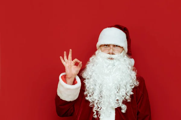 Święty Mikołaj stoi na czerwonym tle i pokazuje swój gest kciuka. Mikołaj i gest. Święta i Nowy Rok. Przestrzeń chroniona — Zdjęcie stockowe