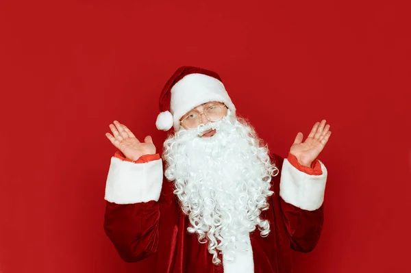 Funny Santa Claus está extendiendo sus manos sobre un fondo rojo. Divertido Santa confundido aislado en rojo. Copiar espacio. Concepto X-mas — Foto de Stock