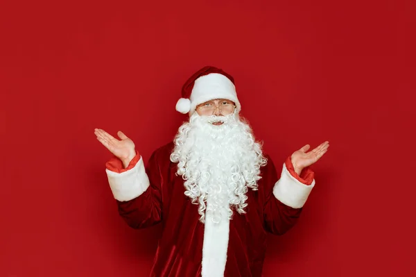 Portrait en studio d'un drôle de Père Noël sur fond rouge, secouant les bras dans la confusion et regardant dans la caméra avec un visage déconcerté. Père Noël confus isolé sur fond rouge. X-mas — Photo