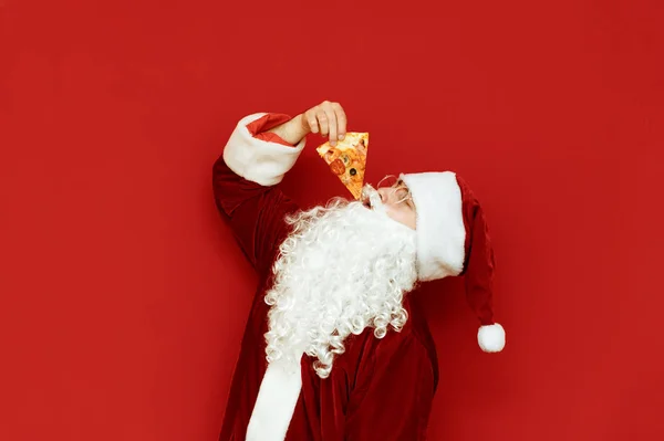 Kırmızı arka planda pizza yiyen beyaz sakallı aç Noel Baba. Noel Baba pizza yemeyi sever, izole edilmiş halde. Komik Noel Baba Pizza Isırıyor. Boşluğu kopyala