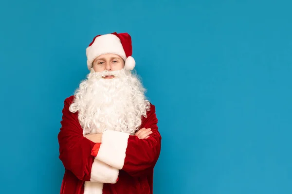 Portret zabawnego młodzieńca w świątecznym stroju karnawałowym Mikołaja, odizolowanego na niebieskim tle, patrzącego w kamerę i uśmiechającego się. Pozytywny, młody Mikołaj pozujący przed kamerą. Przestrzeń chroniona — Zdjęcie stockowe