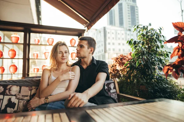 Young stylish couple sitting on terrace in cozy cafe on city bac