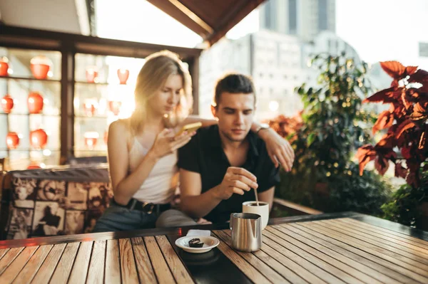 Young couple having dinner in cafe on terrace on sunset background.Young people sitting in restaurant on terrace and drinking coffee.Leisure time with loved one in cafe.Focus on the cup with coffee