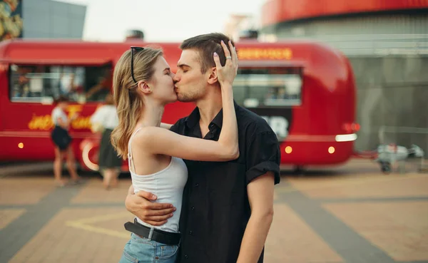Привлекательная молодая пара в стильной повседневной одежде целуется и обнимается на улице на заднем плане фургона с едой. История любви пары, целующейся на свидании, портрет улицы . — стоковое фото