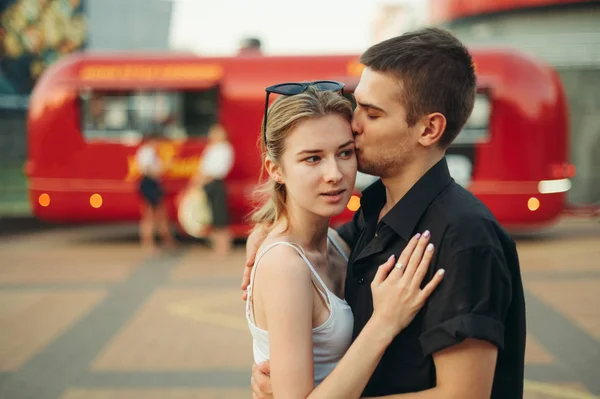 Уличный портрет красивой молодой пары, обнимающей на улице, молодой человек целует девушку в щеку, одевая стильную повседневную одежду. Концепция любви. Дата . — стоковое фото