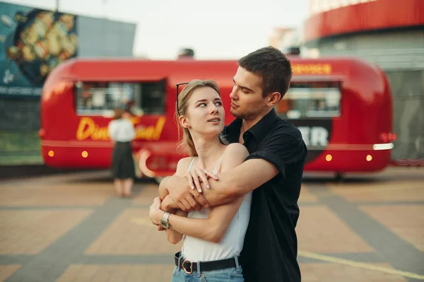 Straat liefdesverhaal foto Jonge koppel knuffelen op een date, staan tegen een achtergrond van een rode voedsel vrachtwagen en kijken naar elkaar in liefde. Liefdesconcept. Valentijnsdag,. — Stockfoto