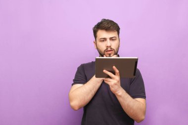 Pembe arka planda duran ve interneti akıllı telefondan kullanan sakallı bir öğrencinin portresi, tabletten dikkatlice okuyor ve öğreniyor. Elinde tablet olan bir adam, izole edilmiş..