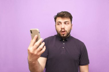 Sakallı, akıllı telefonlu, kafası karışmış, kafası karışık bir adam. Komik adam elinde bir akıllı telefon tutuyor, mor bir arka planda izole edilmiş.