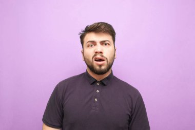 Duygusal sakallı bir adamın yakın plan portresi, kameraya şaşkın bir suratla bakıyor ve kızgın. Mor arka planda şeytani bir yüzü olan koyu renk gömlekli komik bir adam. İzole edilmiş. Adam şokta.