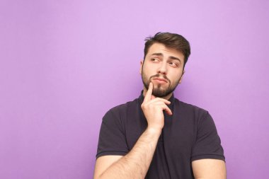 Sakallı ve koyu renk tişörtlü bir adam mor arka planda düşünür ve\ opyspace 'e yan bakar. Düşünceli yetişkin bir adam mor bir arka planda izole edilir..