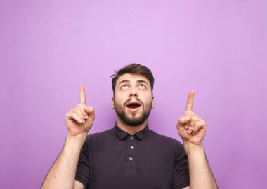 Mor arka planda şaşırmış bir adamın portresi, yukarı bakıyor ve boş bir alanda parmaklarını gösteriyor. Sakallı adam, kopyalanmış, izole edilmiş...