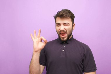 Mor arka plandaki mutlu adam tabelaya gülümsüyor. Sakallı adam neyi sevdiğini gösteriyor, mor bir arka planda izole edilmiş kameraya bakıyor. Yetişkin adam parmak sembolü gösterir.
