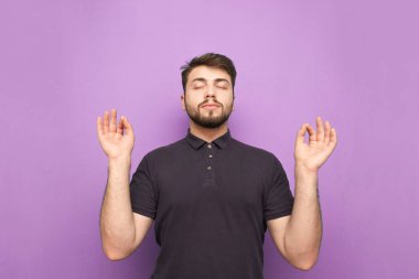 Sakallı sakin bir ofis çalışanı gözleri kapalı ve elleri mor arka planda meditasyon yapar. Adam sakinleşti. İzole edilmiş.