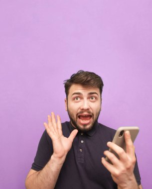 Elinde akıllı bir telefonla mor bir arka planda duran sakallı, şok edici bir yüzü ve boş bir yere bakan ağzı olan deli bir adam. İzole edilmiş. Kopyalama alanı
