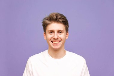 Beyaz tişörtlü gülümseyen genç adam gülümsedi ve kameraya baktı.