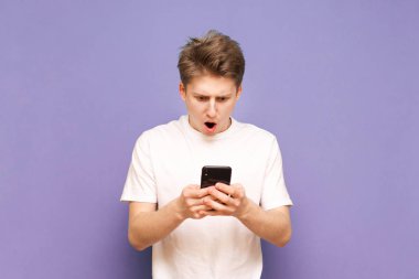 Beyaz tişörtlü genç adam akıllı telefon kullanıyor ve tepki veriyor.