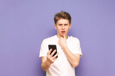 Elinde akıllı bir telefonla duran şaşırmış bir gencin portresi.