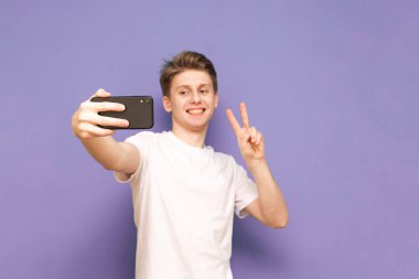 Beyaz tişörtlü mutlu adam akıllı telefondan selfie çekiyor.