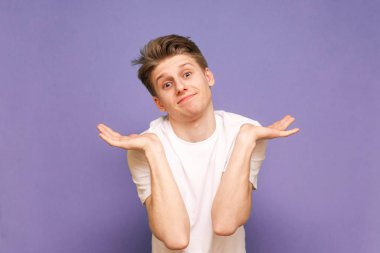 Beyaz tişörtlü komik genç adam mavi bir B 'de kafa karışıklığı gösteriyor.