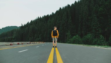 Sarı kazaklı bir erkek yolcunun dağ ormanları manzarasında yolun ortasında durduğunu gördüm. Ormanlık alanda otoyolun ortasında sırt çantalı bir turist vuruldu..