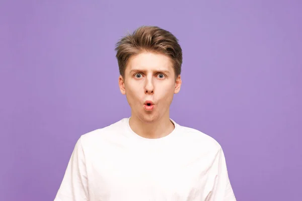 Close up portrait of an adorable guy on a purple background, look into the camera with an open mouth. Emotional young man is isolated on a blue background. — ストック写真