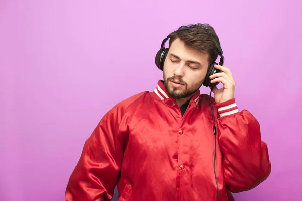 Retrato de close-up de um homem adulto escuta música em fones de ouvido com olhos fechados em um fundo rosa. O entusiasta da música gosta de música. Isolados — Fotografia de Stock