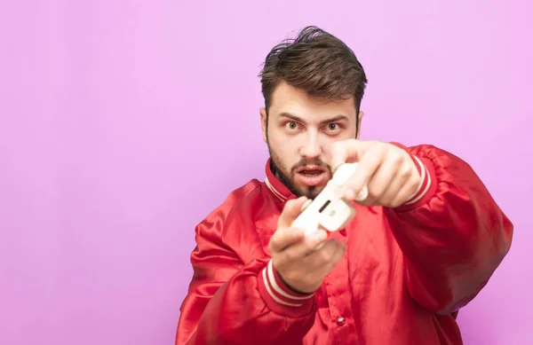 Jogador barbudo focado joga um jogo de vídeo com um gamepad em sua mão e olha para a câmera usando uma jaqueta vermelha. Isolado. Adulto joga um jogo de vídeo, um retrato próximo . — Fotografia de Stock