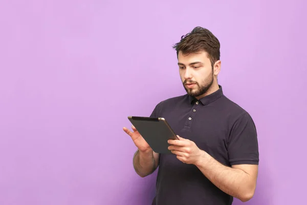 Retrato de um homem adulto concentrado usa a internet em um tablet, vestindo uma barba e uma camiseta escura. Isolado. Homem de negócios com um tablet na mão sobre um fundo rosa . — Fotografia de Stock