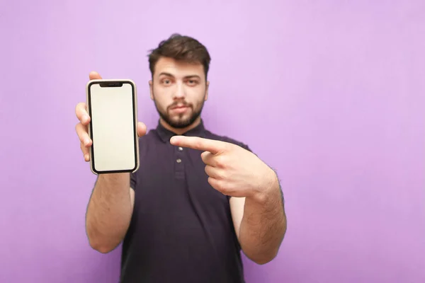 Smartphone with a blank white screen in the hands of an adult man with a beard, wearing a dark shirt and standing on a pink background.Man holds a modern phone in his hands,focus smartphone. Isolated — Stock Photo, Image