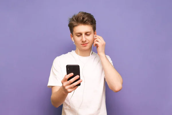 Hermoso joven con una camiseta blanca lleva un teléfono inteligente un —  Fotos de Stock