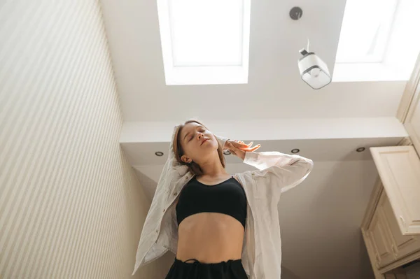 Πορτρέτο της ελκυστική κοπέλα σε casual ρούχα, πρωινή άσκηση στο διαμέρισμα. Χαριτωμένη γυναίκα απολαμβάνει το πρωί με τα μάτια της κλειστά στο διαμέρισμα με φως εσωτερικούς χώρους και φεγγίτες — Φωτογραφία Αρχείου