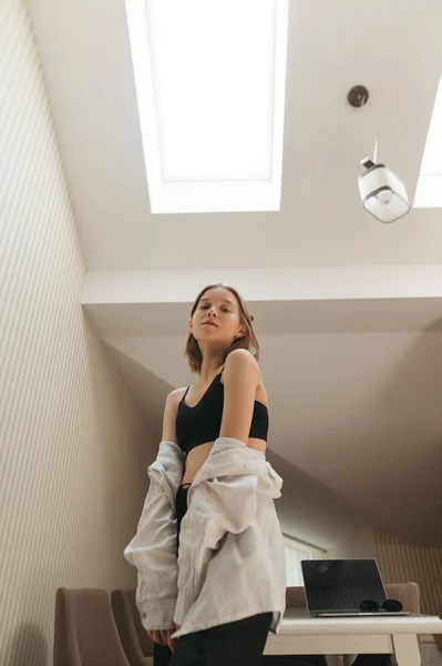 上と白のシャツのセクシーな女の子は、光の屋根裏部屋のアパートでポーズをとって、カメラを見てください。垂直写真. — ストック写真