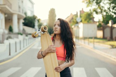 Gün batımında arka planda elinde bir keresteyle dikilen ve gözlerini kaçıran İspanyol bir kızın yakın plan portresi. Kız binici şehirde akşam saatlerinde uzun bir sörf tahtasına biniyor..