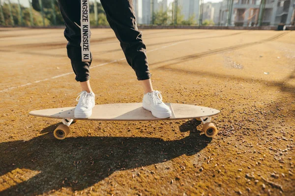 Le gambe della ragazza cavalcano su un longboard nel parco giochi. Ragazza che cammina su un longboard, foto ravvicinata di gambe e tavola. Foto ritagliata. Piedi e skateboard . — Foto Stock