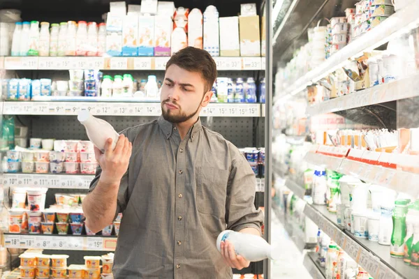 Retrato de un hombre con barba selecciona botella de yogur en una magnífica — Foto de Stock