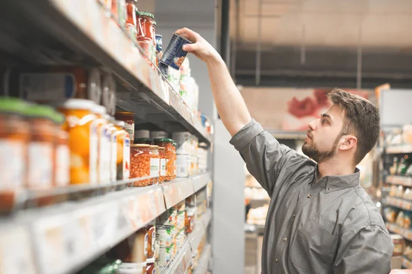 Hombre con barba está en el departamento de conservas de verduras superm — Foto de Stock