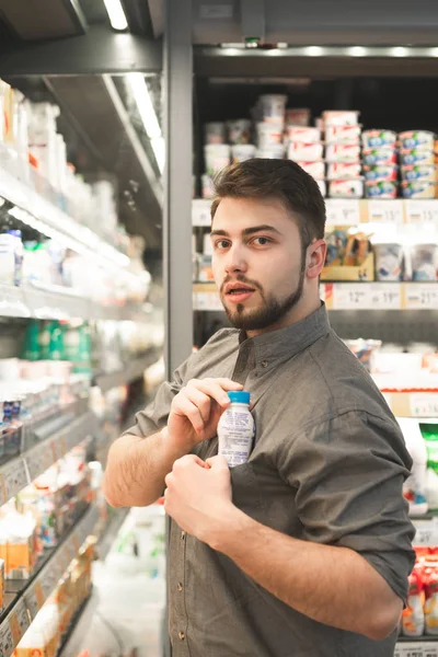 Knappe man staat in de melkafdeling van een supermarkt en — Stockfoto