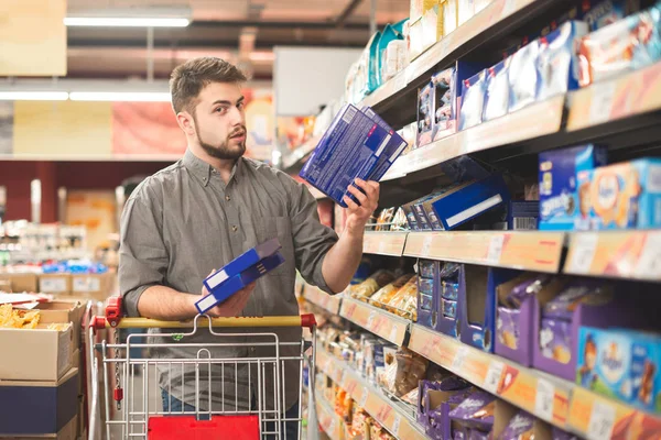 Portrait of confused middle-aged man doing grocery shopping in supermarket: calling his wife asking what dessert to choose — Stock Photo, Image