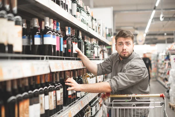 これは大丈夫だよ。ワインのボトルを押しながらのワイン店に立ちながら見てハンサムな若者の側面図 — ストック写真