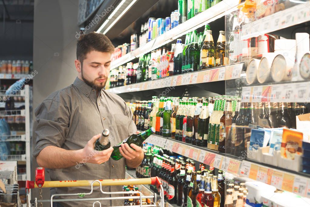 Man with a beard stands in a supermarket in an alcoholic departm