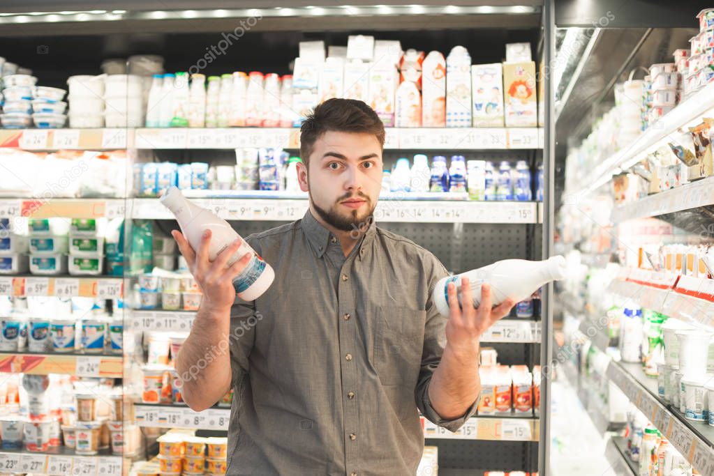 Man is standing with two bottles of milk in the milk department 