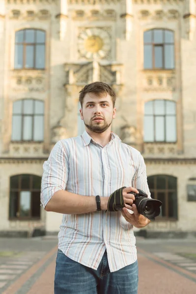 Portré vonzó férfi fotós kültéri európai építészeti háttér. Fiatal jóképű férfi szakáll tartja kamera a kezében, hogy komoly és átgondolt. — Stock Fotó